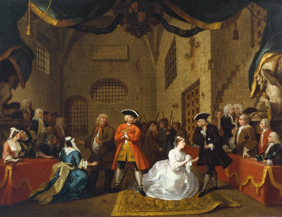 A crowded prison scene from John Gay's ballad opera, the players in eighteenth-century dress, a standing man in a red coat and leg irons at the centre with a kneeling woman on either side of him.
